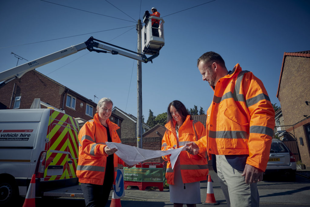 Three CityFibre engineers looking at plans on a street while an engineer is looking at telephone wires